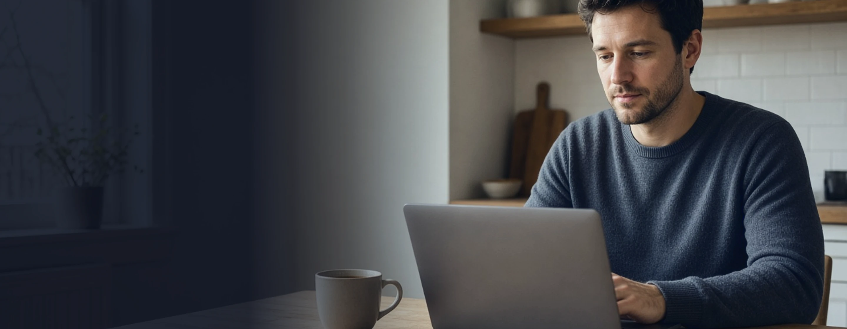 Man at his kitchen table on a laptop, filling in a short form